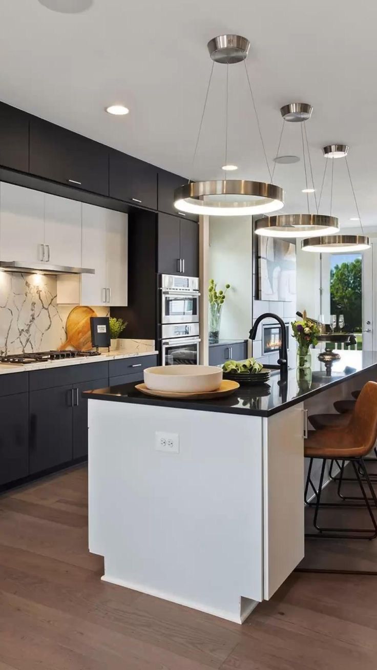 Modern kitchen with black and white cabinetry, a black countertop island with brown chairs, and three circular pendant lights.