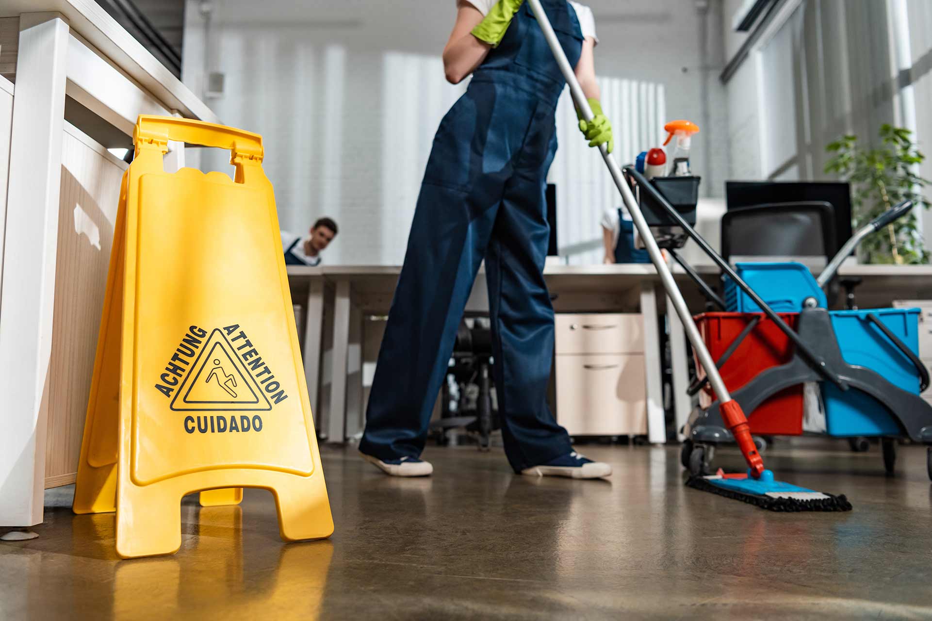 Janitor mopping floor in an office with a yellow caution wet floor sign nearby.
